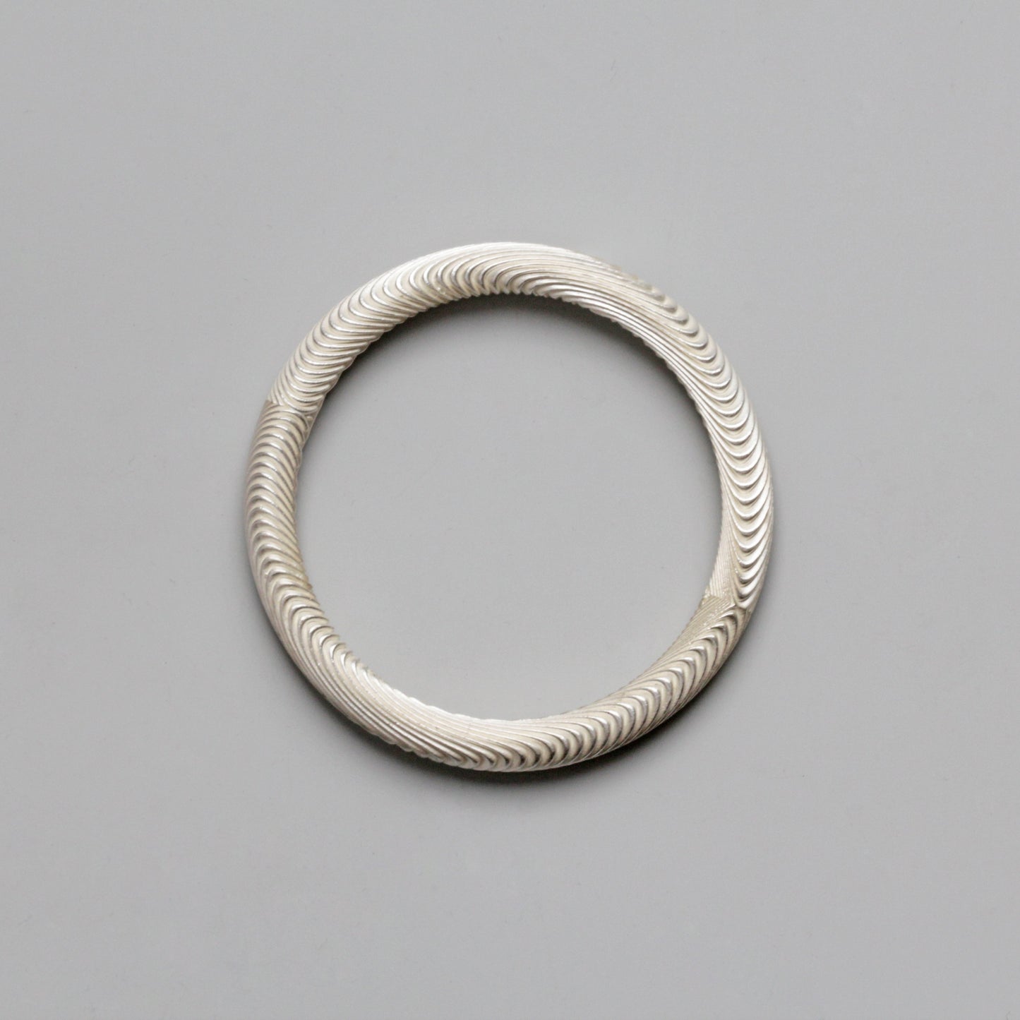 Silver bracelet with wavy pattern on a gray background