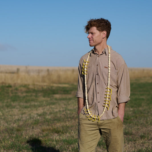 Man standing in a field wearing suspenders with a clear blue sky background