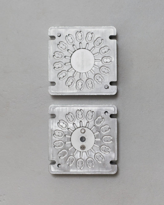 Two metallic square plates with circular designs on a gray background