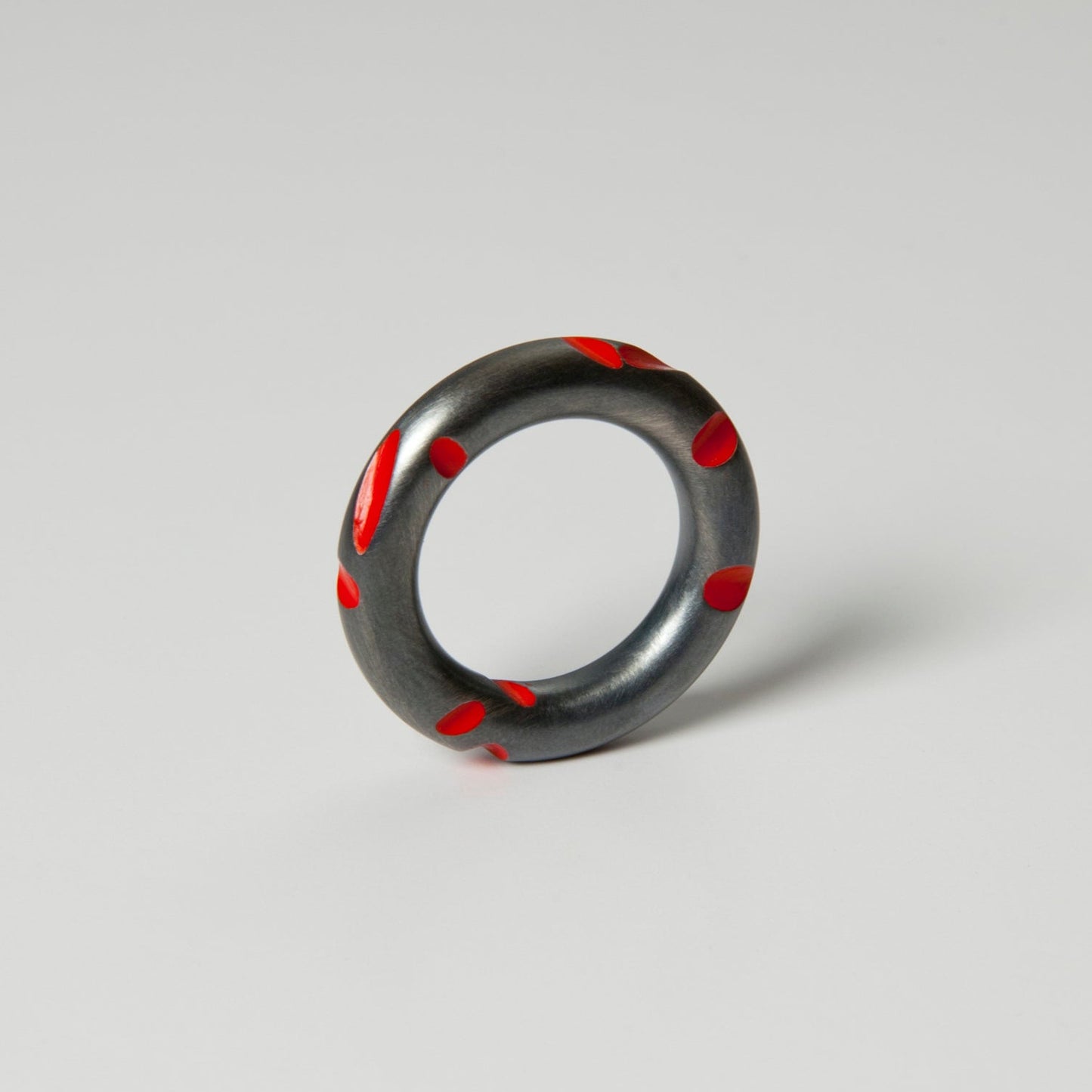 A blackened silver ring with red lacquered details on a plain background.