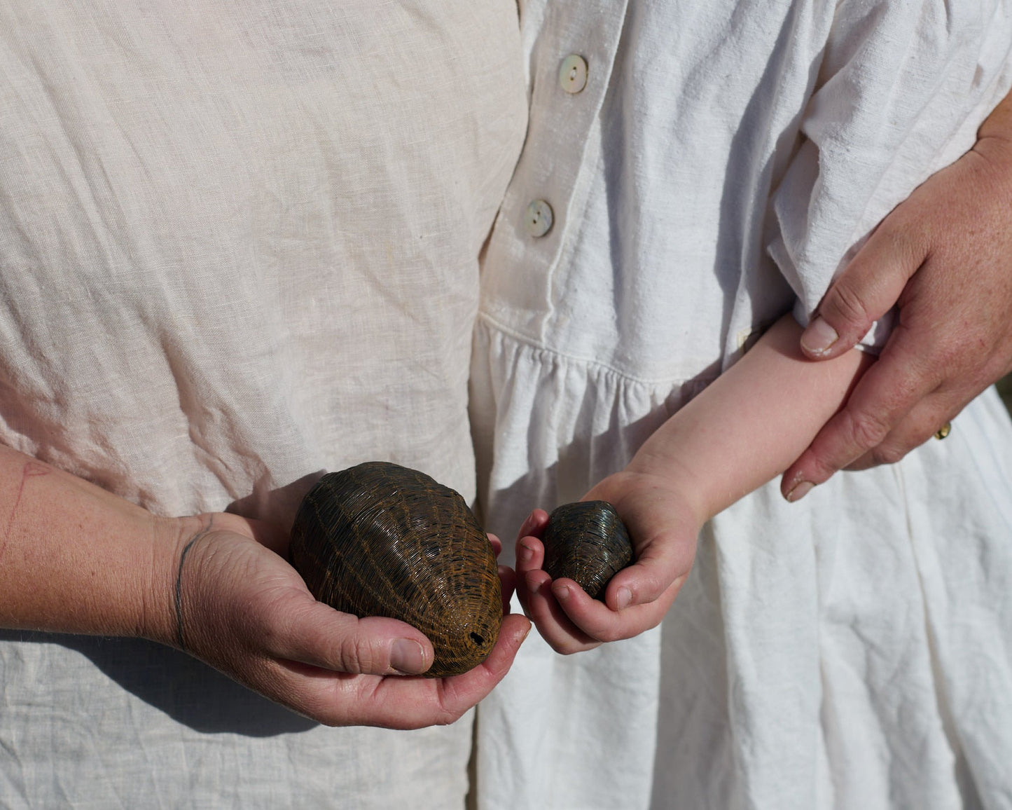 Two people holding stones outdoors, wearing white dresses.