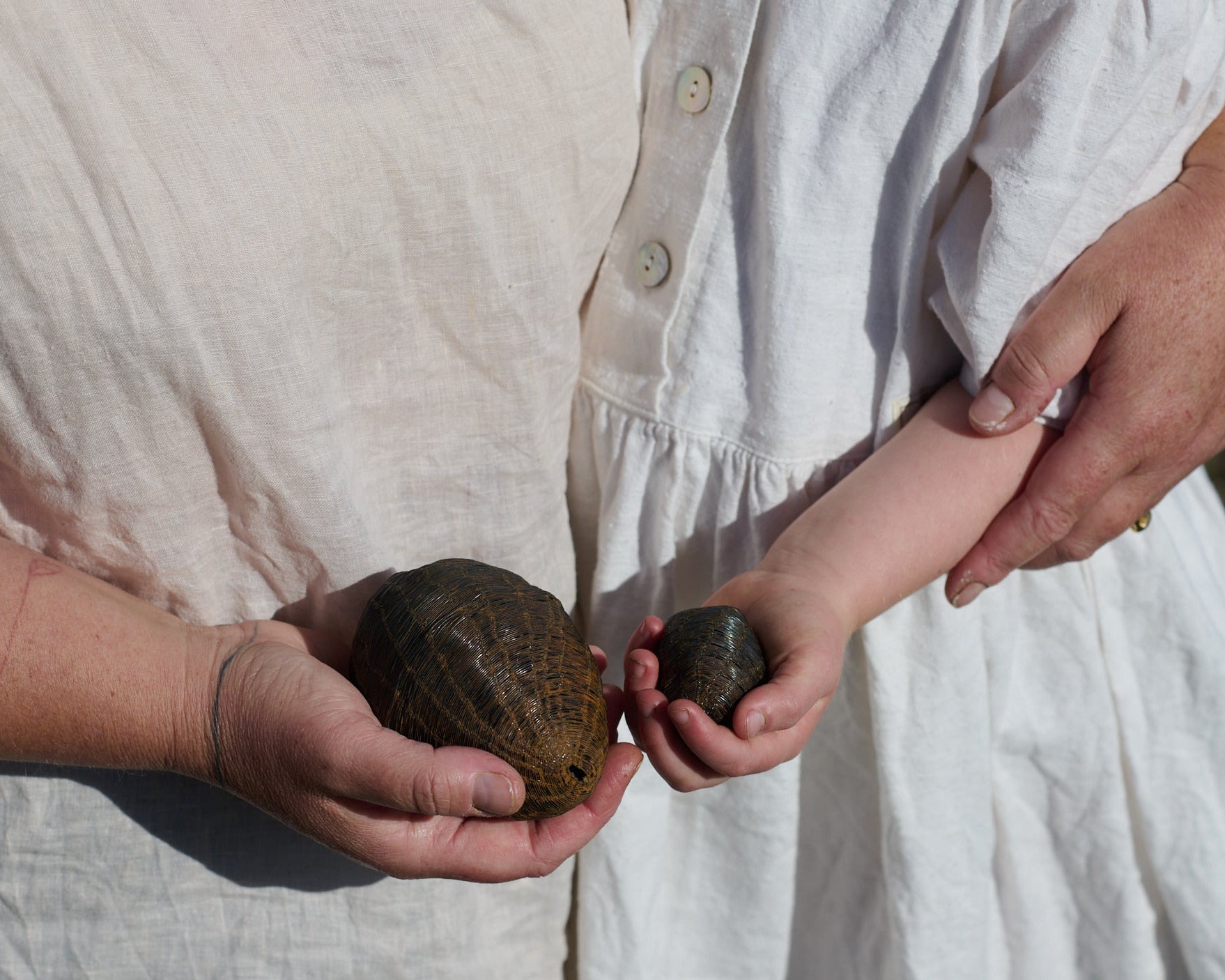 Two people holding stones outdoors, wearing white dresses.