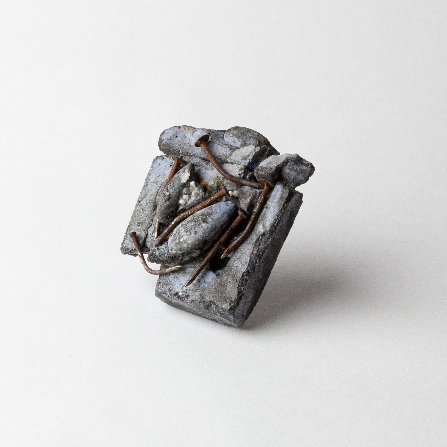 A small sculptural ring with a textured, abstract metallic design in silver and gray tones, featuring thin copper wire details, photographed on a clean light gray background.