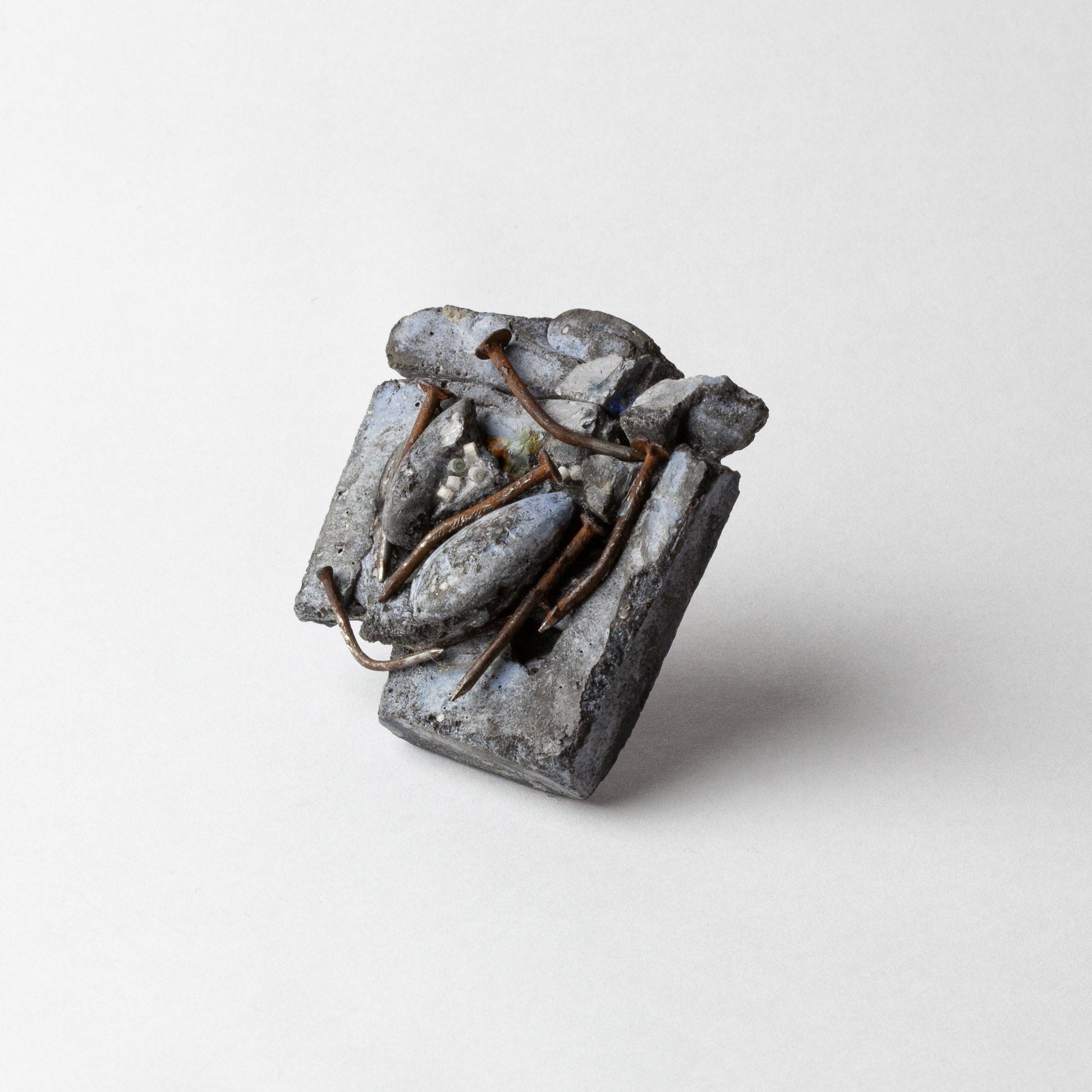 A small sculptural ring with a textured, abstract metallic design in silver and gray tones, featuring thin copper wire details, photographed on a clean light gray background.