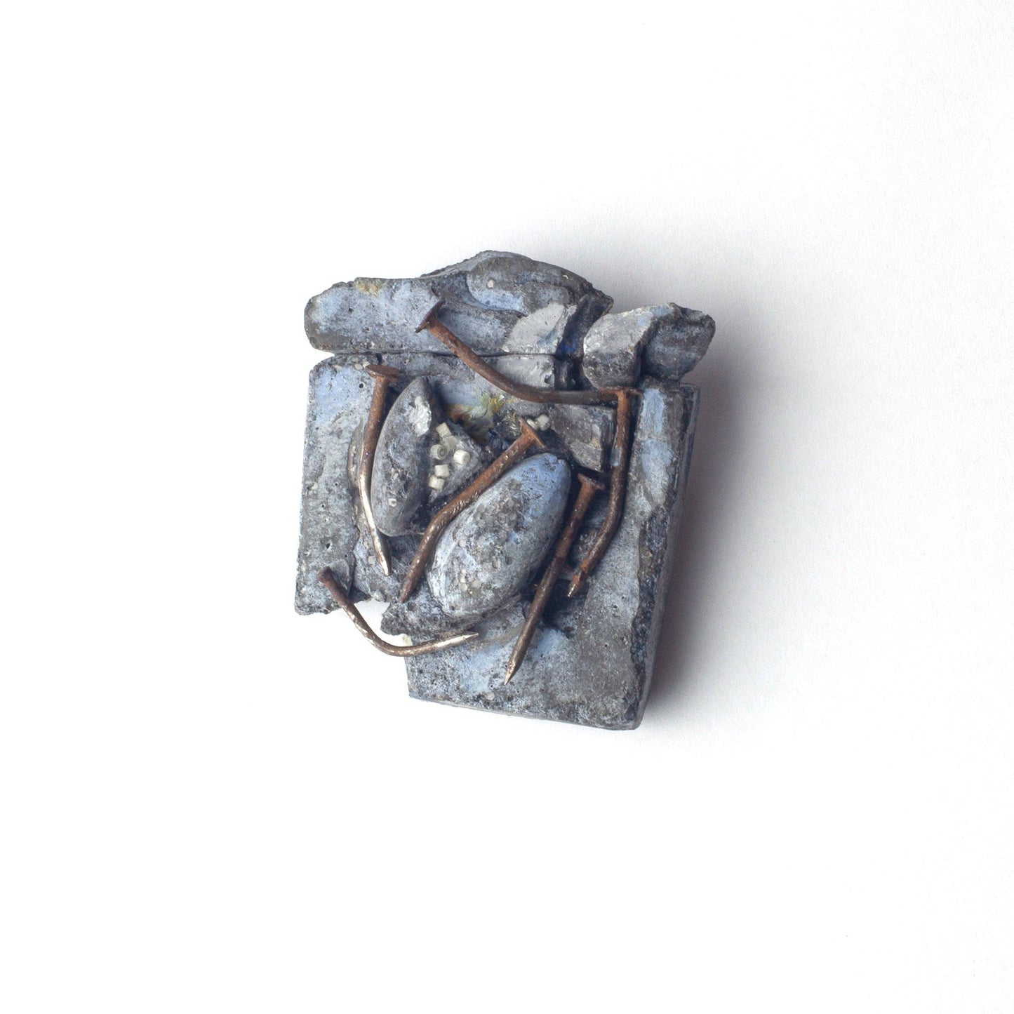 A small abstract sculptural object with layered metallic gray and silver forms and thin copper-toned wire details, photographed on a plain white background.