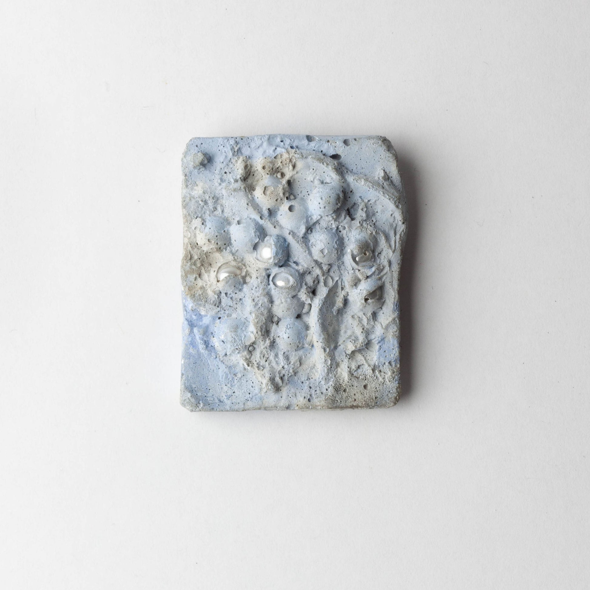 A square handmade ceramic brooch with a textured, organic surface featuring light blue, gray, and white marbled patterns, photographed against a clean white background.