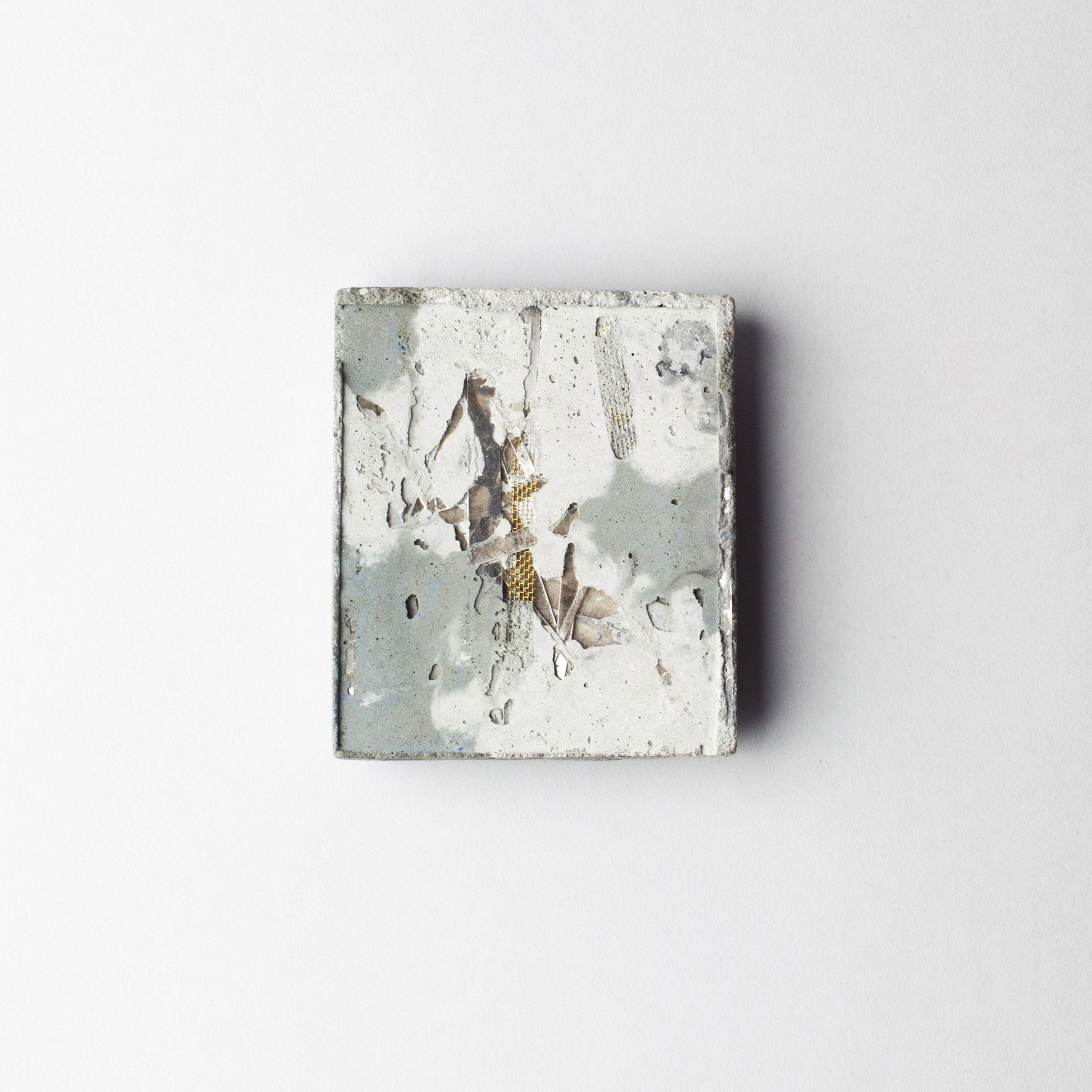 A square abstract art print or tile featuring textured splashes of gray, white, and metallic gold, centered on a clean white background.