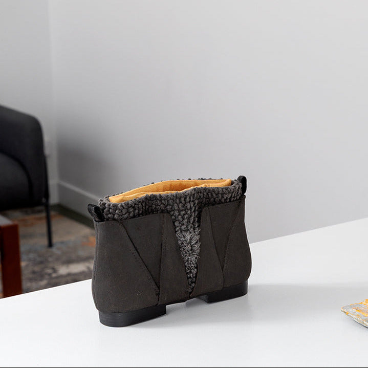 A pair of textured ankle boots in dark brown and orange, displayed on a white table alongside a matching orange pouch and small blue accessories against a minimalist white wall background.
