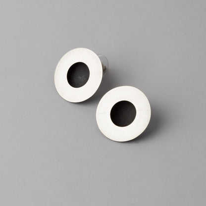 Pair of earrings with white circular design and black center on a gray background