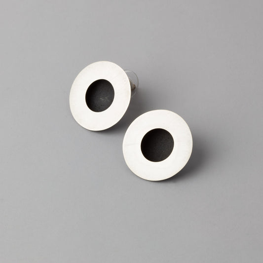 Pair of earrings with white circular design and black center on a gray background