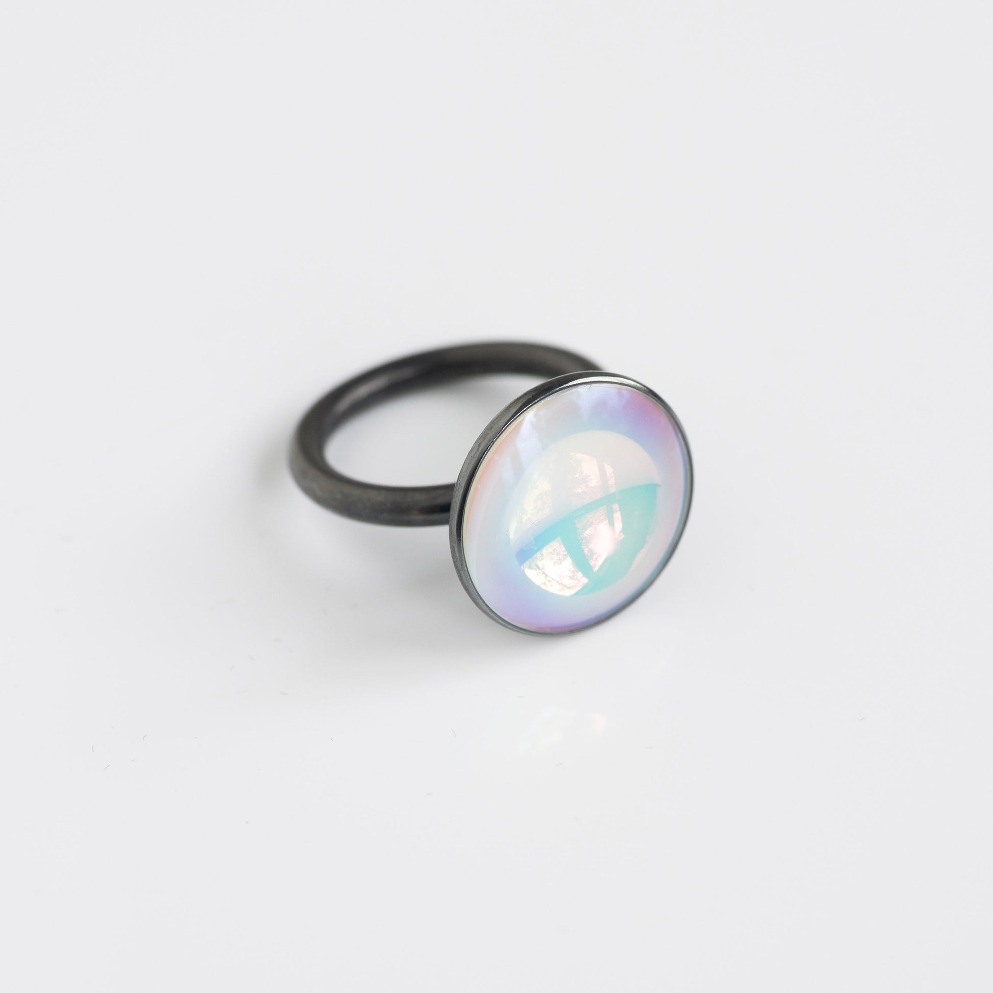 Ring with a round, iridescent gemstone on a light gray background
