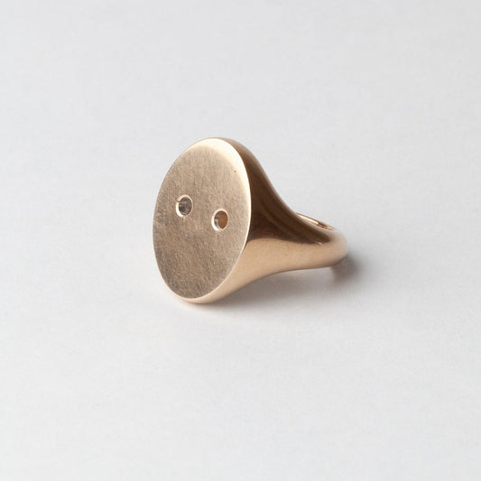 Gold ring with a round face on a light gray background