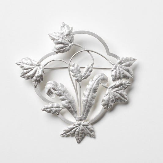 Decorative silver brooch with floral design on a white background