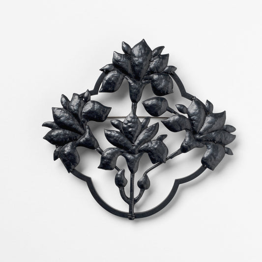 Decorative metal brooch with leaf design on a white background