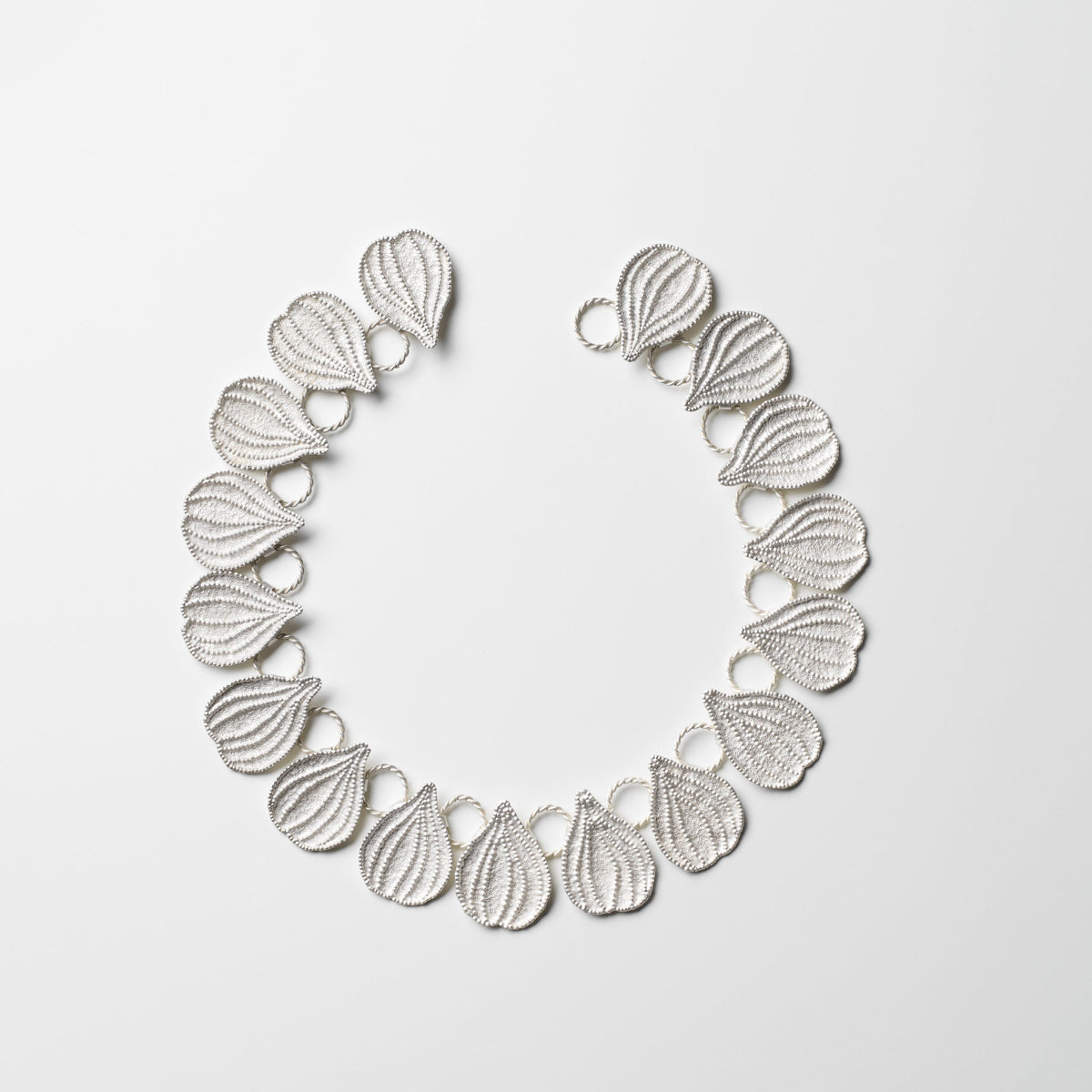 Silver necklace with leaf-like design on a light gray background