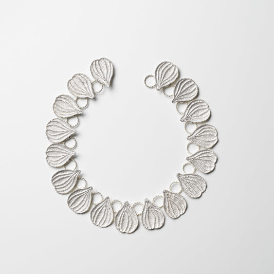 Silver necklace with leaf-like design on a light gray background