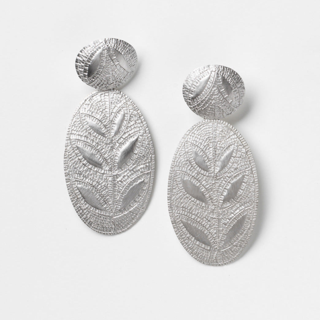 Pair of silver leaf-patterned earrings on a light gray background