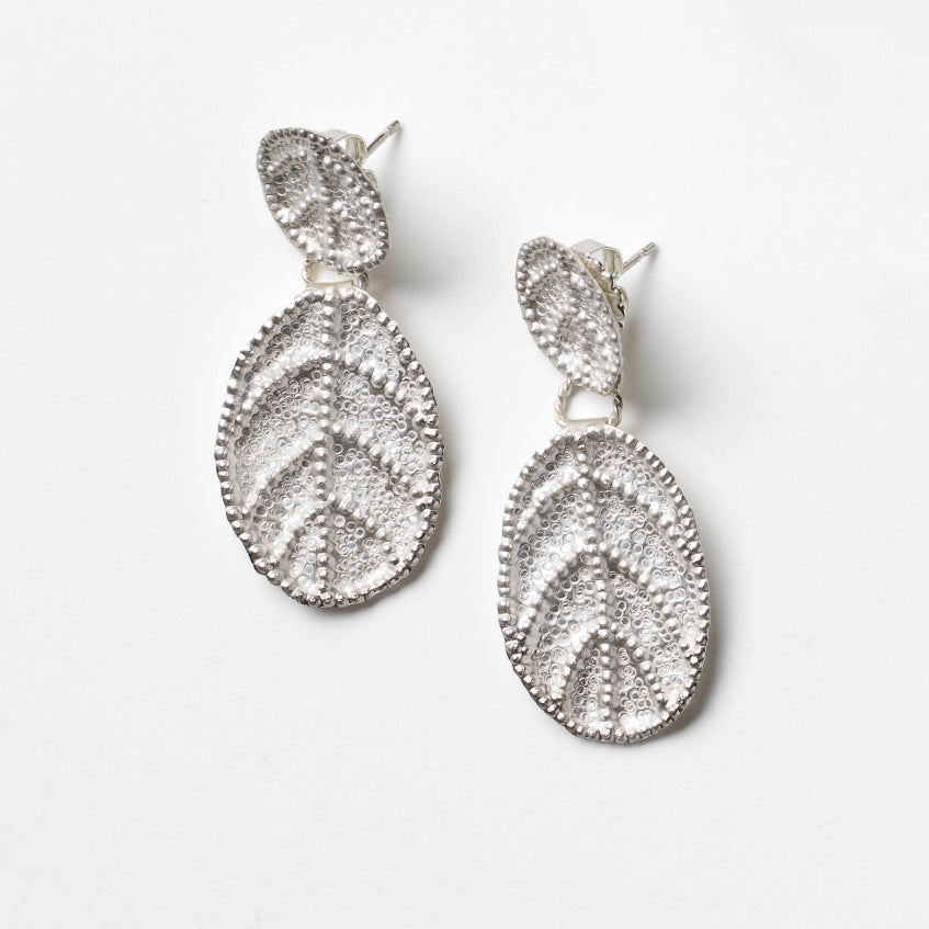 Pair of silver leaf-shaped earrings on a light gray background