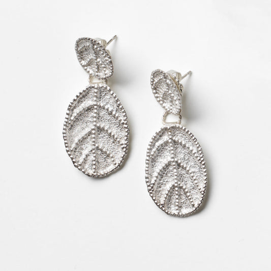 Pair of silver leaf-shaped earrings on a light gray background