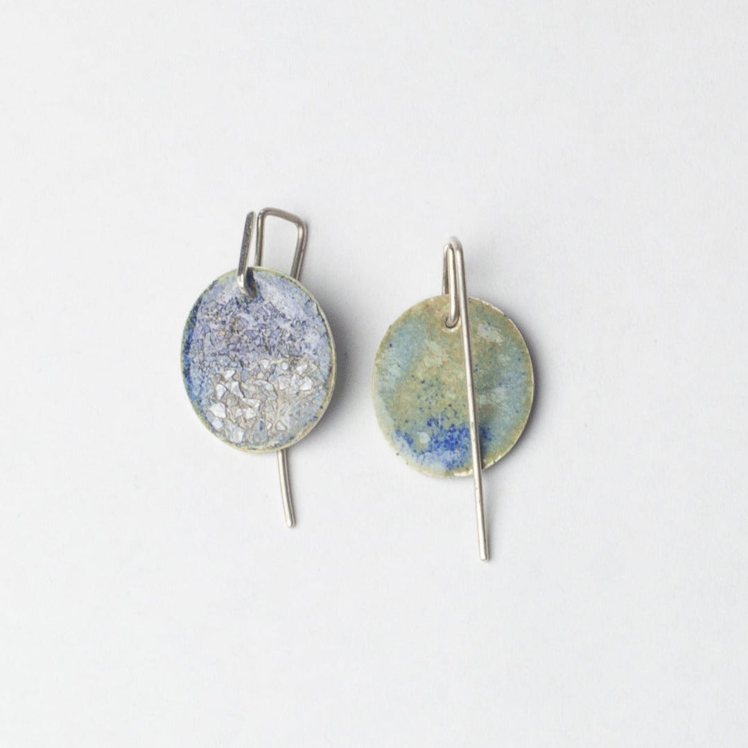 Pair of earrings with round, textured discs on a light gray background