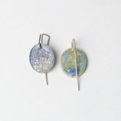 Pair of earrings with round, textured discs on a light gray background