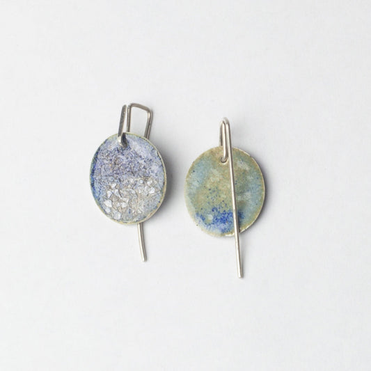 Pair of earrings with round, textured discs on a light gray background